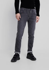 Vaqueros de mezclilla gris con un ajuste slim y textura desgastada, con trabillas para cinturón, bolsillos delanteros y dobladillos enrollados, combinados con zapatos deportivos negros.