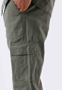 Pantaloni cargo verde oliva realizzati in un tessuto testurizzato, con tasche laterali e una tasca a pattina sulla coscia con dettagli di cucitura discreti.