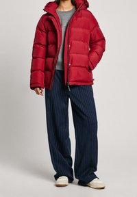 Röd puffjacka med huva, dragkedjestängning och boxig design. I kombination med marinblå rutiga vida byxor och vita sneakers.