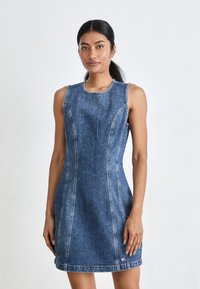Denim uten ermer kjole med en tettsittende fasong, lys blå farge, subtile rhinestones og søm-detaljer langs kantene.