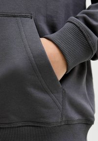 Felpa grigia con polsini e bordo a coste, tasca frontale singola e texture liscia con dettagli di cucitura visibili.