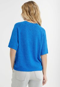 Kurzärmliger blauer Strickpullover mit entspanntem Schnitt und geripptem Saum. Texturiertes Gewebe mit leicht lockerer Webart.