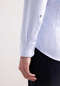 Camicia a quadretti blu chiaro e bianca con polsini abbottonati, caratterizzata da un piccolo dettaglio ricamato sulla manica, realizzata in cotone.