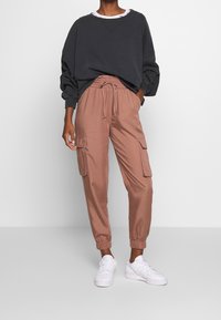 Tummanharmaa ylipitkä collegepaita leveillä hihoilla, yhdistetty vaaleanruskeisiin cargo-housuihin, joissa on joustavat resorit lahkeissa ja kaksi sivutaskua. Valkoiset lenkkarit.