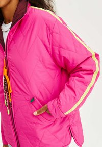Prošívaná růžová bunda s žlutým pruhem, bočními kapsami a nastavitelným stahováním s dekoračními prvky na výstřihu.