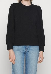 Svart stickad tröja med rund halsringning, figurnära överdel och puffärmar. Texturerad tyg med ribbade mudd och fåll. Bärs med ljusblå jeans.