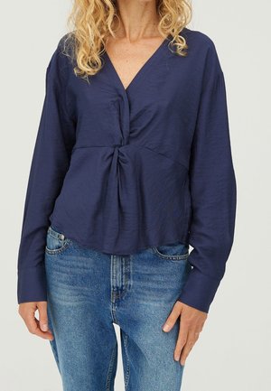Navyblaue Bluse mit langen Ärmeln, tiefem V-Ausschnitt und gewundener Vorderseite. Der Stoff wirkt glatt mit einer leicht gekräuselten Textur.