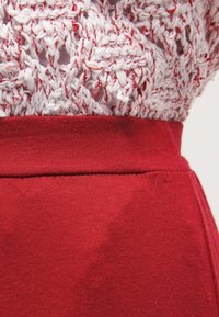 Top in maglia con un motivo a filato attorcigliato bianco e rosso, abbinato a una cintura in tessuto rosso uniforme e a una gonna, con una consistenza liscia.
