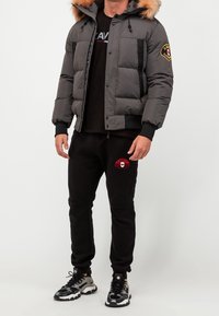 Gray puffer jacket with a fur-lined hood, zip and snap closure, black accents, paired with black joggers featuring a red logo and textured detail.