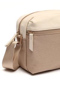 Beige kabelka přes tělo s hladkým koženým vrškem, texturovaným tkaninovým spodkem, horním zipovým uzávěrem a nastavitelným popruhem. Kompaktní a praktický design.