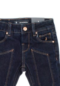 Jeans in denim blu scuro con cuciture arancioni, cinque tasche e vita con bottoni. Etichetta che riporta "JECKERSON" con taglia "18".