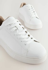 Baskets blanches avec dessus en cuir lisse, bout rond, fermeture à lacets et accents beiges au niveau du talon et de l'intérieur. Semelle en caoutchouc texturé.