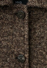 Abrigo marrón con patrón de espiga, que presenta una tela texturizada, un cuello con muesca y un cierre de botón negro de cuatro agujeros. Etiqueta de la marca visible.