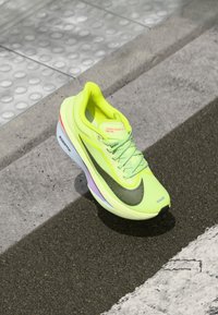 Bright yellow Nike Zoom Fly shoe with mesh upper, black Swoosh, reflective accents, and a cushioned sole featuring a multicolored midsole.