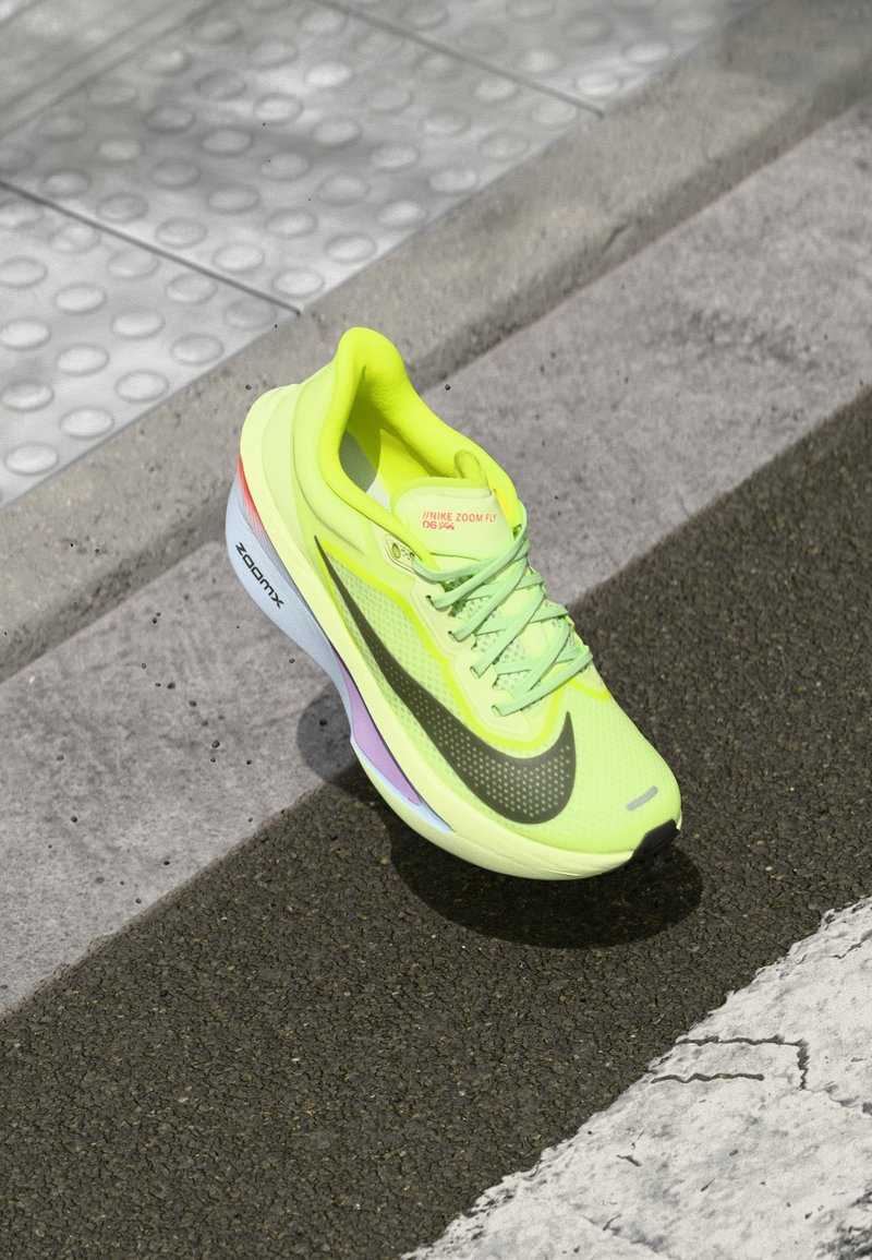 Bright yellow Nike Zoom Fly shoe with mesh upper, black Swoosh, reflective accents, and a cushioned sole featuring a multicolored midsole.