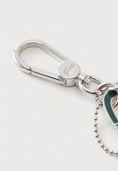 Porte-clés mousqueton en métal argenté avec un fermoir circulaire montrant un petit logo crocodile embossé.