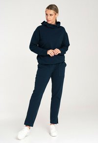 Granatowy hoodie z kapturem, zestawiony z pasującymi spodniami cargo z bocznymi kieszeniami i luźnym krojem. Całość dopełniają białe trampki.