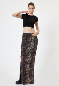 Maxikleid mit Leopardenmuster und hohem Schlitz, aus leichtem Stoff. Es zeigt dunkle und helle Brauntöne auf schwarzem Hintergrund.