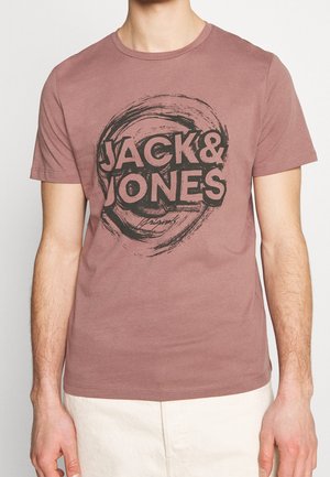 Homme portant un t-shirt à manches courtes rose poudré avec le texte "JACK & JONES" et un motif circulaire de coups de pinceau sur le devant.