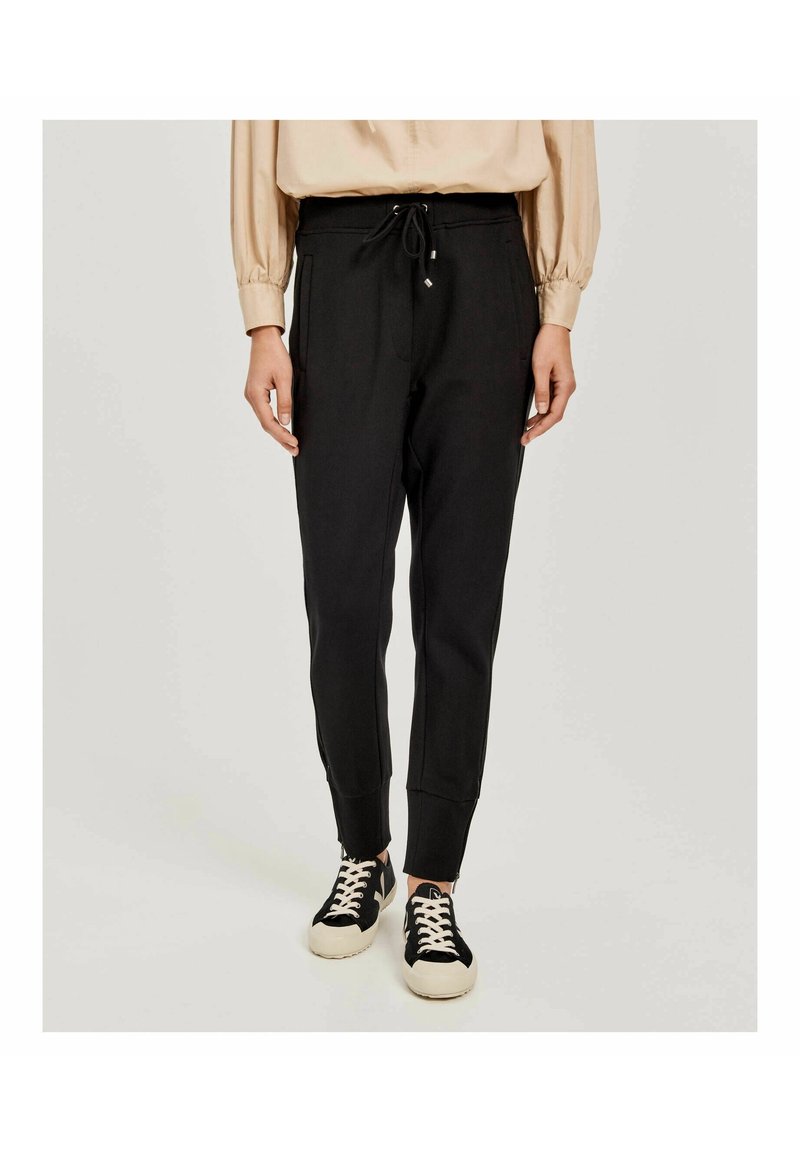 Schwarze Jogginghosen mit einem Kordelzugbund, seitlichen Taschen und gerippten Bündchen, aus einem weichen Material. Kombiniert mit schwarz-weißen Sneakers.