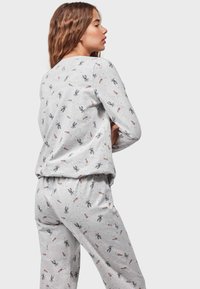 Conjunto de pijama en gris claro que incluye una camiseta de manga larga y pantalones con estampado. El diseño presenta ilustraciones de conejitos y zanahorias en toda la tela.