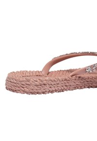 Růžové žabky s texturovanou tkanou podrážkou a hladkými popruhy, které mají řadu jasných krystalů podél horního okraje.