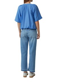 Top azzurro chiaro a maniche corte con dettaglio arricciato sulla schiena abbinato a jeans azzurri chiari a gamba dritta con orli sfilacciati e sneakers beige.