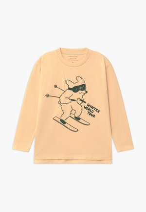 Chemise beige à manches longues avec un dessin au trait noir d'un chien skieur portant des lunettes et le texte « Winter World Tour. »