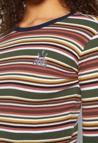 Gestreiftes Baumwollhemd mit grünen, rosa, weißen und braunen horizontalen Streifen; navy-blauer gerippter Ausschnitt; gesticktes Logo auf der Brust.