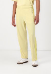 Pantalones de chándal amarillos claros, hechos de una tela suave, que cuentan con un corte ajustado, cinturilla elástica, bolsillos laterales y rayas laterales amarillas en contraste.