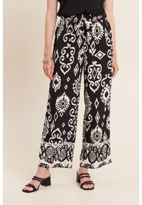 Zwart-witte gestreepte wijde broek met een trekkoord in de taille. Bevat ingewikkelde ontwerpen van diamanten en krullen. Het materiaal lijkt licht van gewicht.