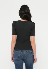 Zwarte nauwsluitende top met korte, opgepofte mouwen, ronde halslijn en gladde textuur, gecombineerd met blauwe spijkerbroek.