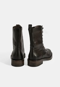 Zwarte leren enkellaarzen met een gestructureerde afwerking, ronde neus en een gestapeld houten hak. Voorzien van zijveters en een lus aan de achterkant.