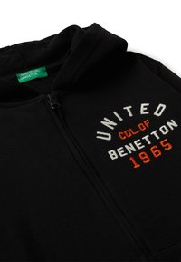 Felpa nera con zip, caratterizzata da ricamo "UNITED COLORS OF BENETTON 1965" in bianco e arancione. Tessuto morbido con dettaglio sul cappuccio.