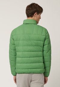 Giacca imbottita verde con colletto alto, caratterizzata da un design trapuntato e sezioni orizzontali, texture liscia e polsini elastici.