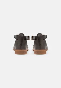 Schwarze Ledersandalen mit Knöchelriemen und einem Holzabsatz. Das Design umfasst Aussparungen für Atmungsaktivität und minimale Hardware-Akzente.