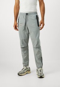 Light grey athletic pants with elastic waistband, black zipper pockets, and Paris logo. Made from lightweight fabric, featuring a tapered design.