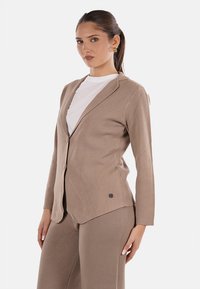 Blazer beige a maniche lunghe con revers a punta, chiusura a un bottone e tessuto testurizzato; presenta un accento con il marchio vicino all'orlo.