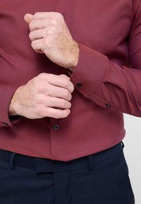 Bordeaux gemusterd overhemd met een gestructureerde weving, lange mouwen en knoopmanchetten, gecombineerd met marineblauwe broek.
