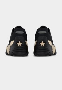 Μαύρα αθλητικά παπούτσια με υφή στο επάνω μέρος, που διαθέτουν μπεζ λεπτομέρεια και αστέρι στο τακούνι. Στρογγυλεμένο σχήμα.