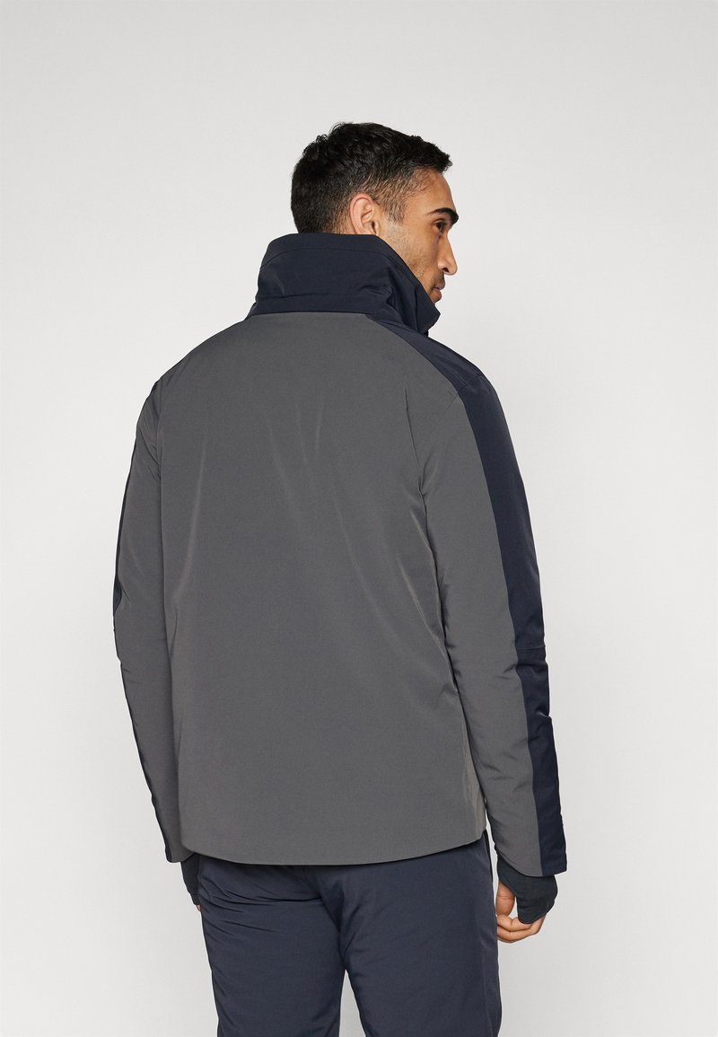 Giacca grigia e blu navy con colletto alto, caratterizzata da una superficie liscia e texture, e pannelli per le braccia a contrasto, progettata per caldo e comfort.