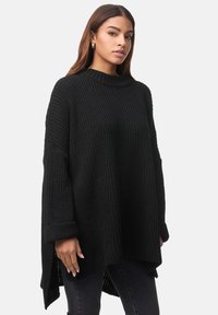 Zwarte gebreide trui met een gestructureerde weefsel, hoge hals, lange mouwen en zijsplitten. Gecombineerd met donkere jeans voor een gelaagde uitstraling.