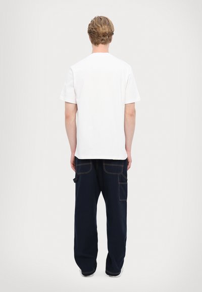 Tricou alb din bumbac cu mâneci scurte, asortat cu pantaloni cargo largi de culoare bleumarin, având buzunare laterale și cusături în contrast.