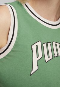 Top in cotone verde senza maniche con collo a costine in bianco e nero, caratterizzato da un audace logo "Puma" stampato in bianco sul davanti.