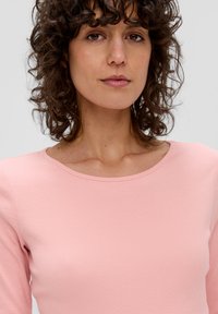 Roze geribbelde longsleeve met een ronde hals. De stof lijkt zacht en aansluitend, wat de textuur van het oppervlak benadrukt.