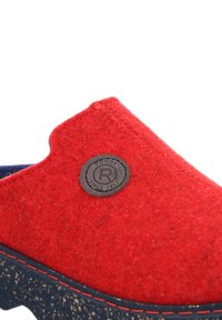 Red wool slip-on shoe with a textured surface, featuring a round, dark button logo and contrasting dark sole with red stitching accents.