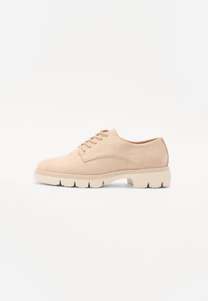 Zapato de ante beige con cordones, puntera redondeada, parte superior texturizada y suela de goma gruesa con surcos definidos para mayor tracción.