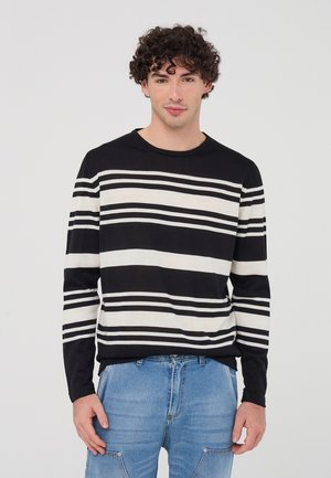 Maglietta a maniche lunghe a strisce bianche e nere con scollo tondo, abbinata a jeans in denim azzurro chiaro. Tessuto testurizzato con strisce orizzontali.
