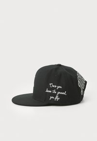 Fekete snapback sapka vászonból; fehér hímzett szöveggel a fronton és az oldalon, lapos szélekkel. A szöveg így hangzik: "Miután elhagyod a talajt, repülsz."
