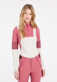 Ružový a biely fleecový zipsový top s dlhými rukávmi. Vlastnosti vzorovanej časti na rukávoch a priliehavého strihu. V kombinácii s ružovými nohavicami.